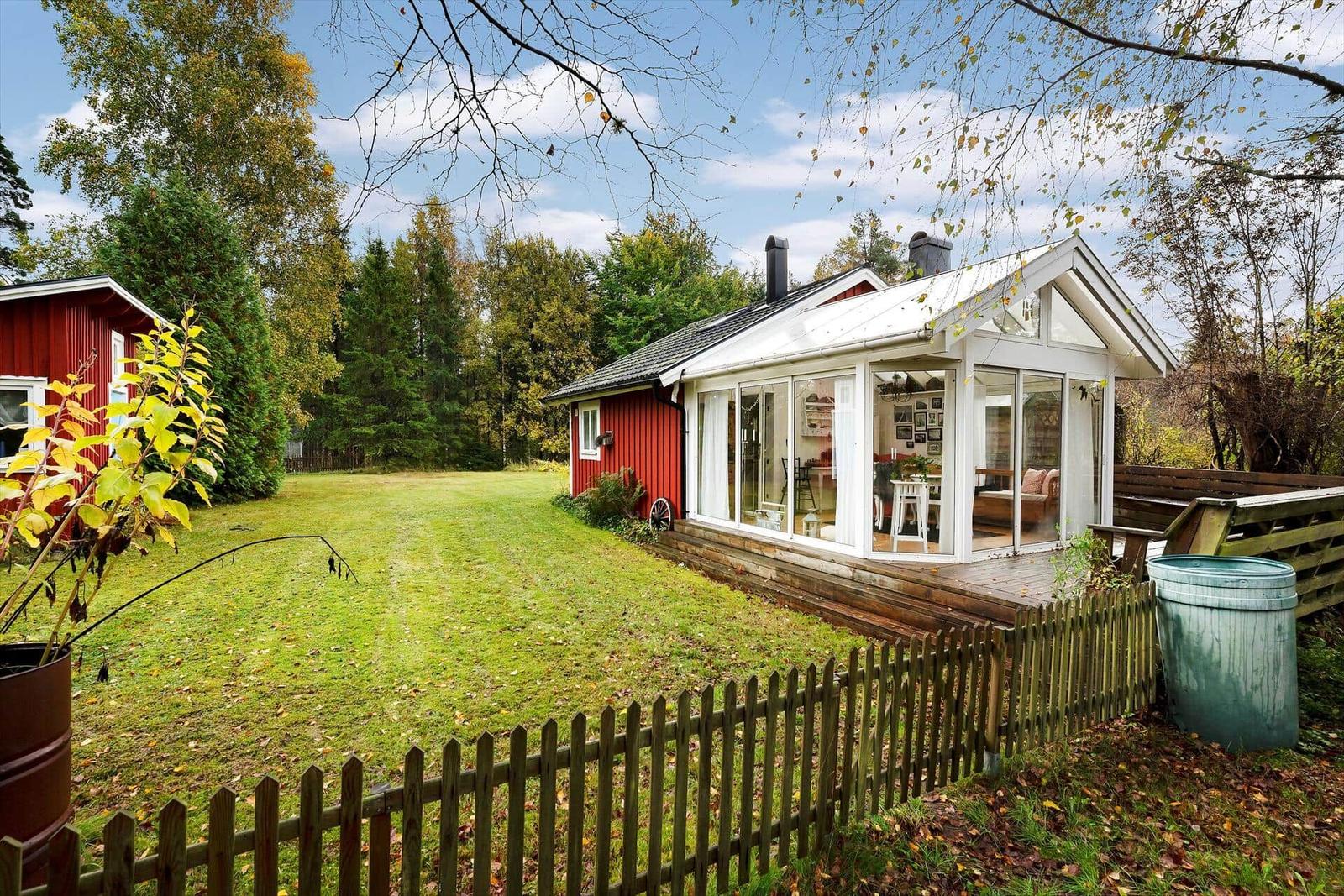 Rotes Holzhaus mit Glasfront und Holzterrasse im Grünen.