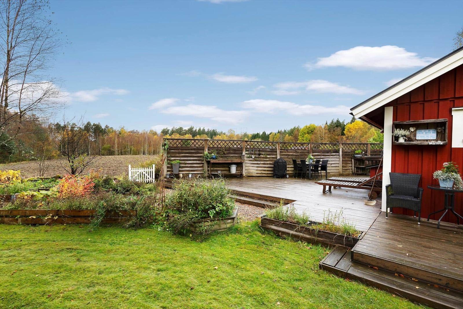 Roter Holzschuppen mit Terrasse, Garten und Blick auf Wald.
