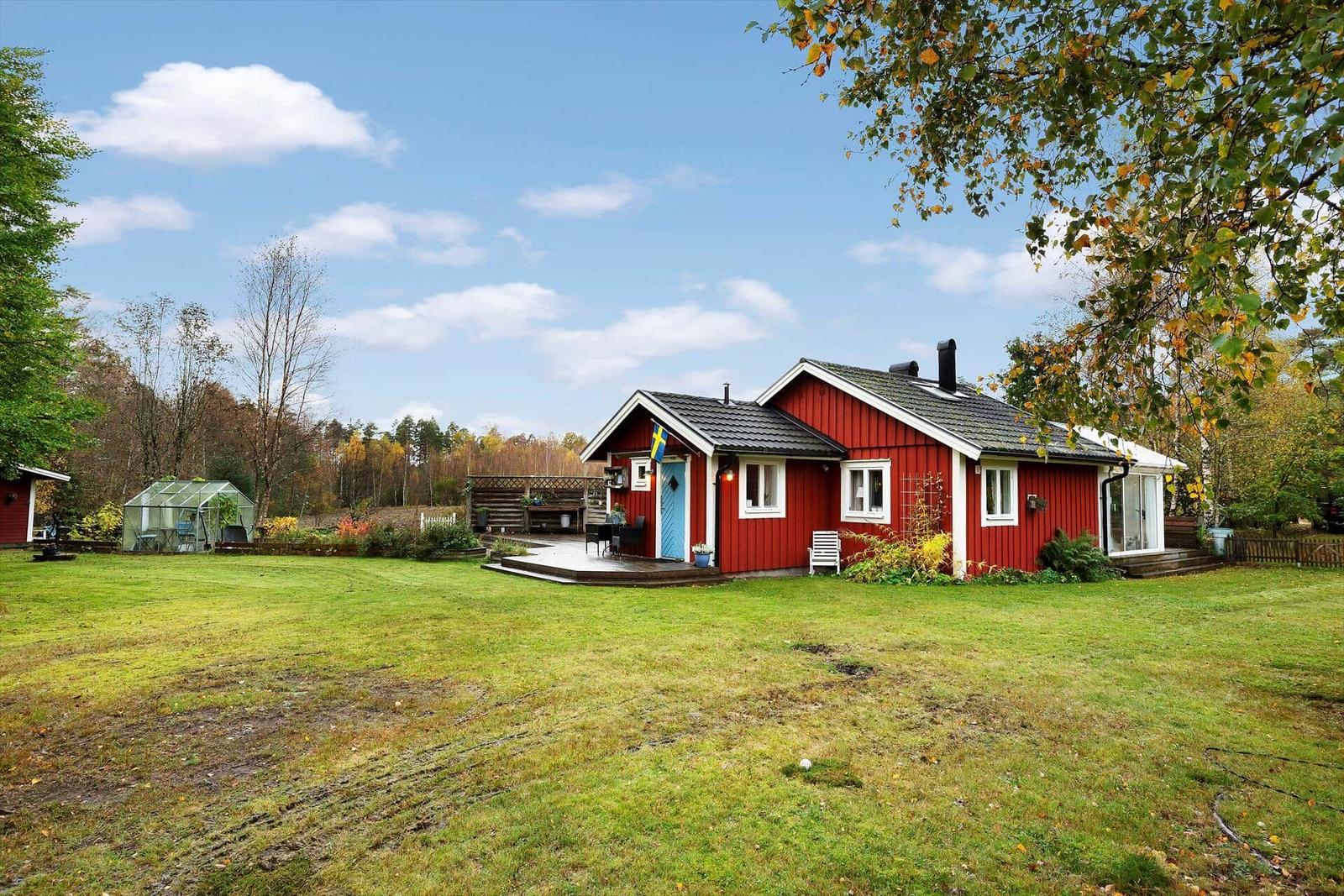 Rotes Holzhaus mit blauer Tür und Terrasse im Garten.