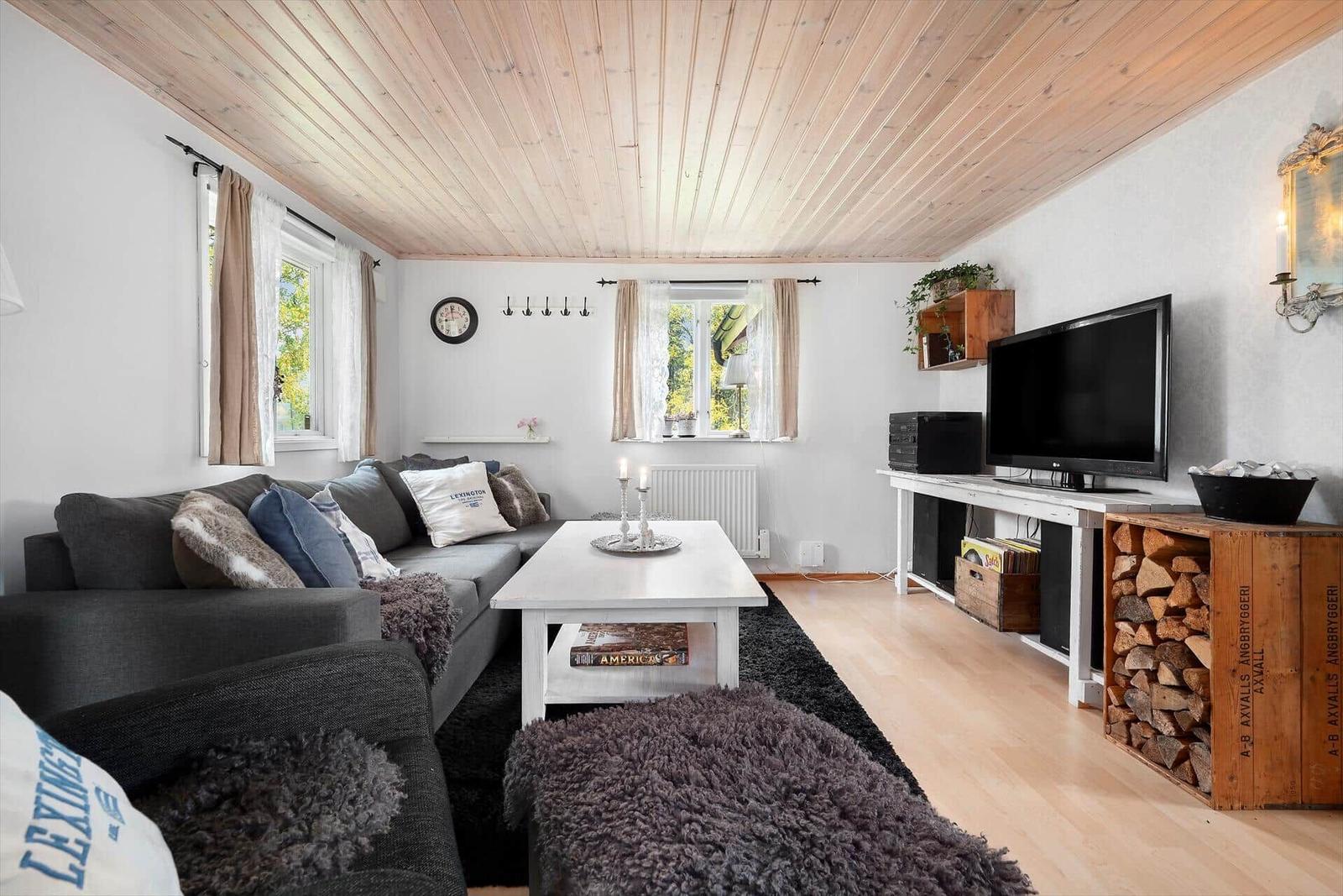 Wohnzimmer mit Sofa, Couchtisch und Fernseher. Holzdecke und Kaminholz.