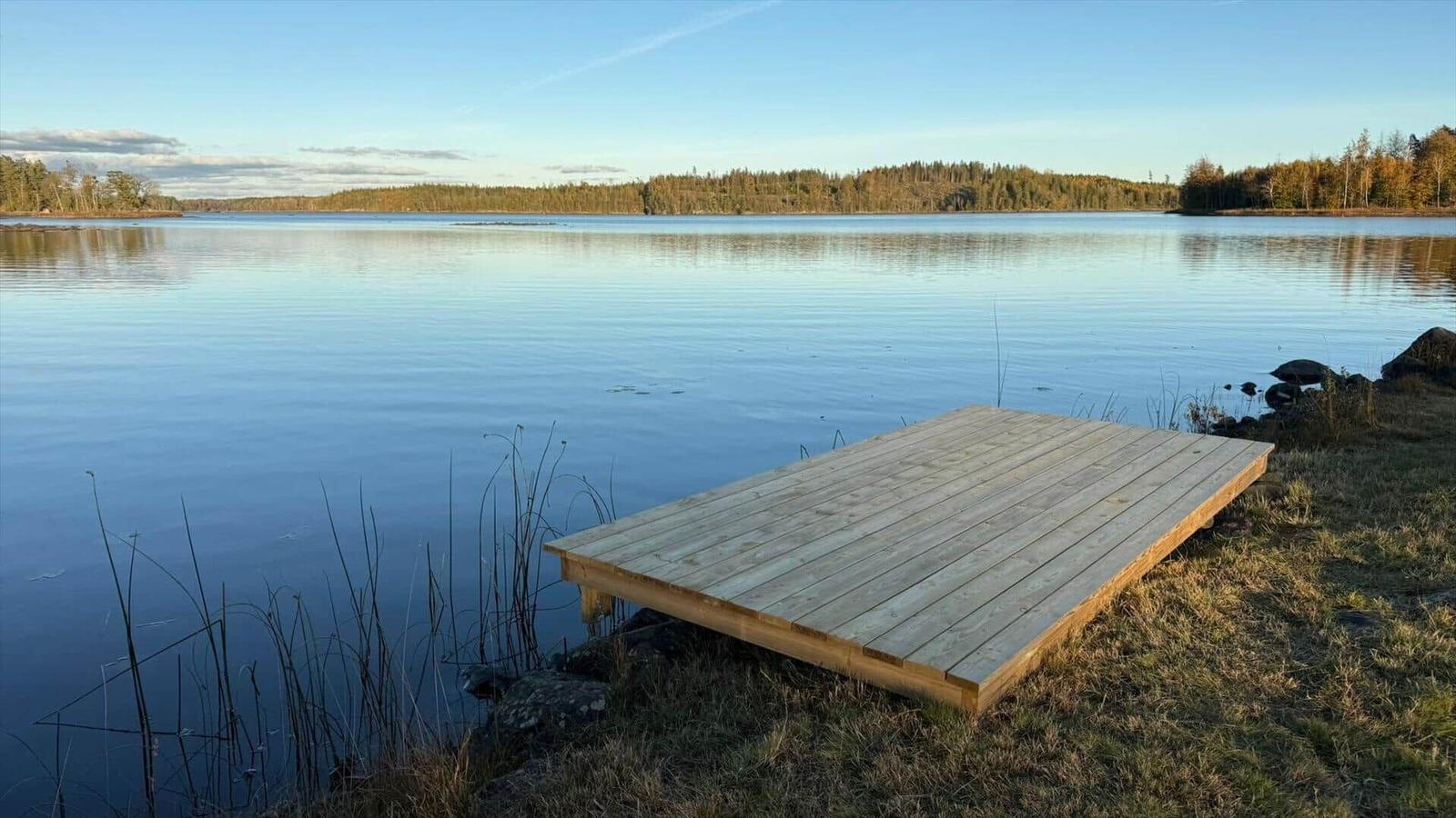 Holzterrasse am ruhigen Seeufer mit Blick auf Wald und Wasser.