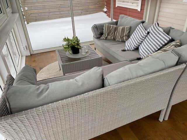 Terrassenbereich mit grauem Rattan-Sofa und Tisch. Hintergrund: Schnee und Holzwand.