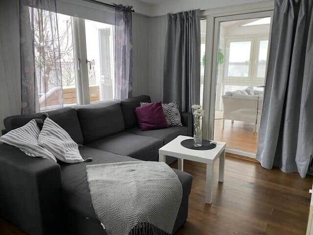 Ein Wohnzimmer mit grauem Sofa, weißem Tisch und großen Fenstern.