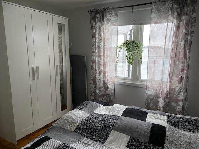 Schlafzimmer mit Bett, Kleiderschrank und Fenster mit Vorhängen.