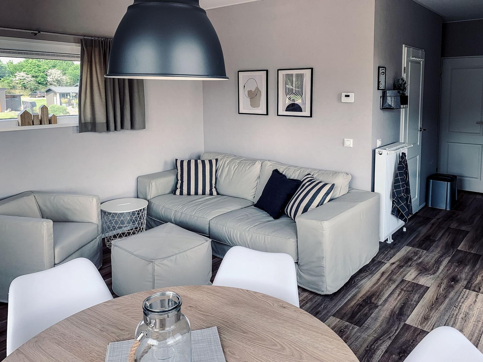 Wohnbereich mit Sofa, Sessel und Esstisch. Fenster mit Blick nach draußen.