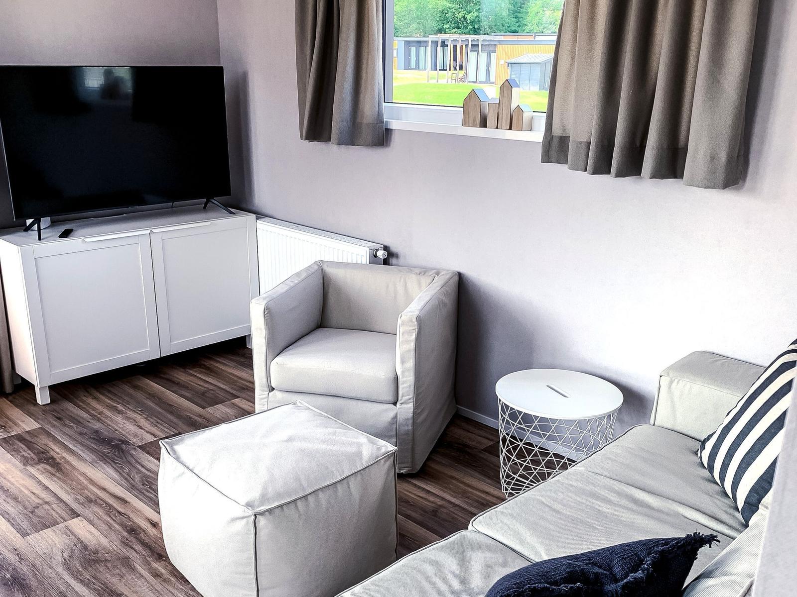 Wohnzimmer mit Sofa, Sessel und Fernseher. Fenster mit Blick auf Garten.