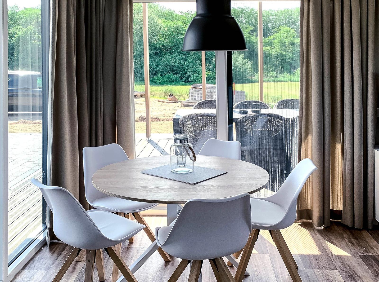 Runder Tisch mit vier Stühlen vor großem Fenster mit Blick auf Terrasse.