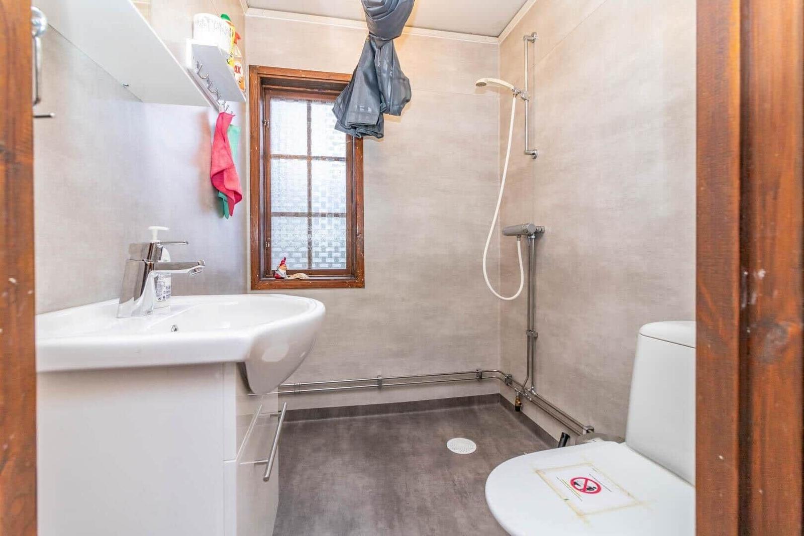 Badezimmer mit Waschbecken, Dusche und Toilette. Fenster mit Holzrahmen.