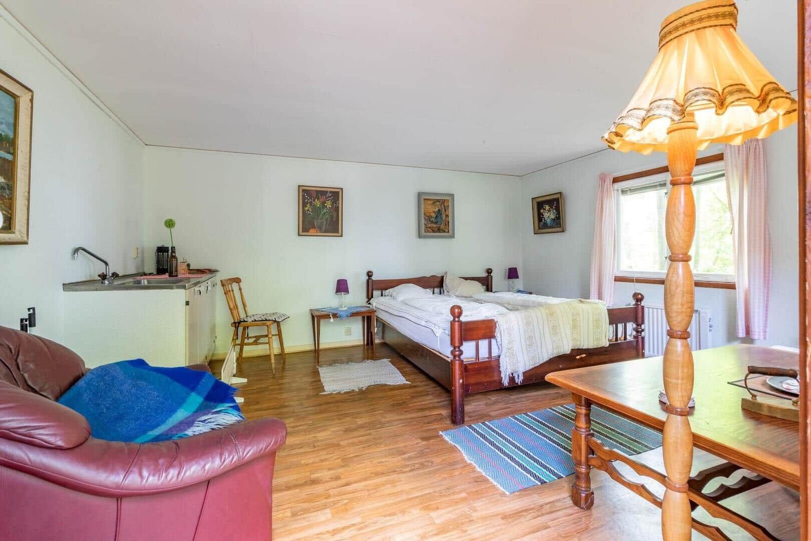 Ein Schlafzimmer mit Bett, Tisch, Stuhl und Küchenzeile. Holzboden und Fenster mit Vorhängen.