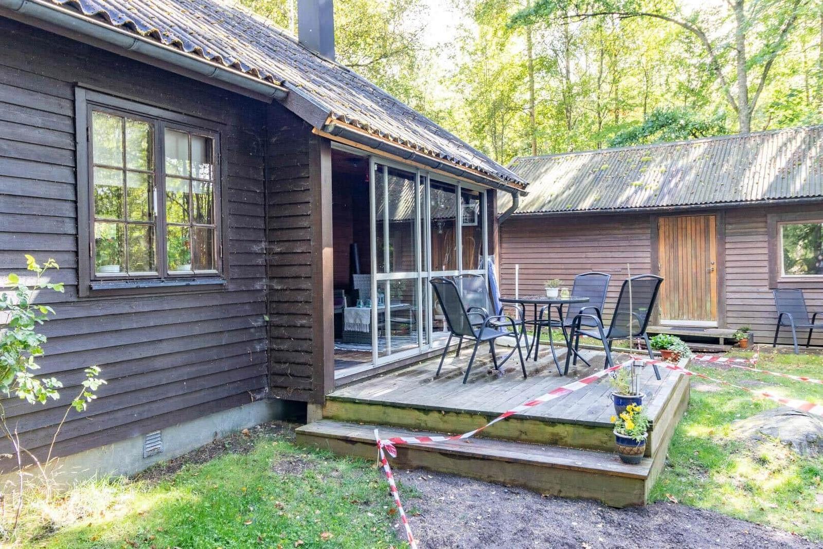 Holzhaus mit Terrasse und Garten. Sicht auf Schlauch und Tisch.