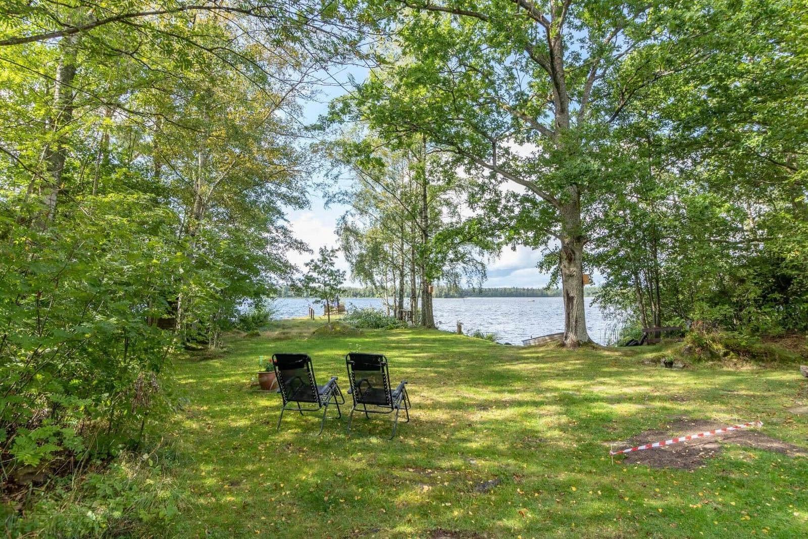 Zwei schwarze Liegestühle auf grünem Rasen unter Bäumen am See.