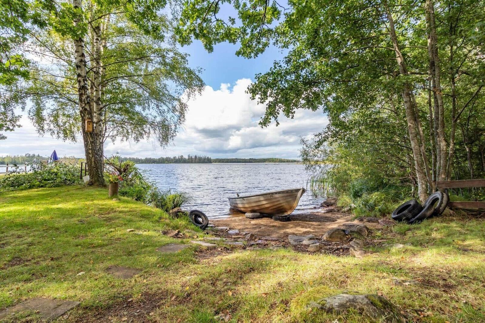 Ein kleines Boot liegt am Ufer eines Sees unter Bäumen.