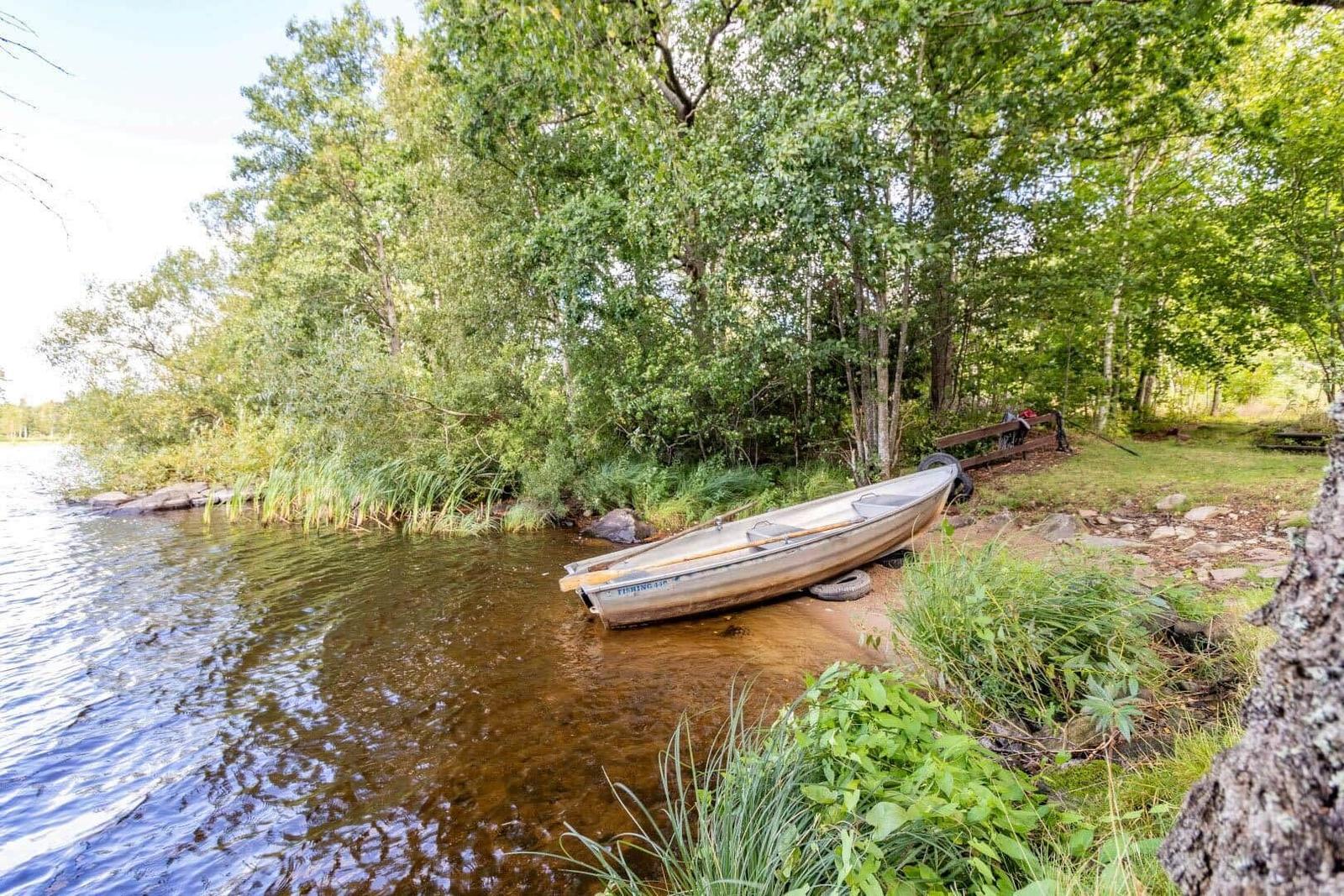 Ein kleines Boot liegt am Ufer eines Sees, umgeben von Bäumen und Gras.