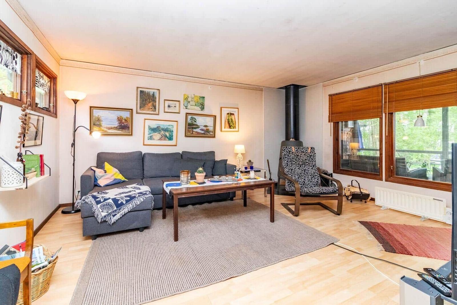 Wohnzimmer mit Sofa, Couchtisch und Kaminofen. Fenster mit Holzjalousien.