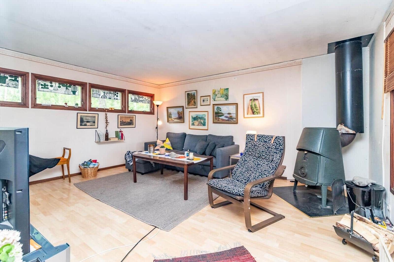 Wohnzimmer mit Sofa, Sessel und Kaminofen. Holzboden und Fenster mit Buntglas.