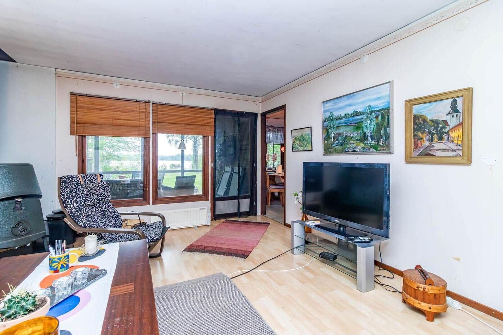 Wohnzimmer mit TV, Fenstern und Gemälden an der Wand.