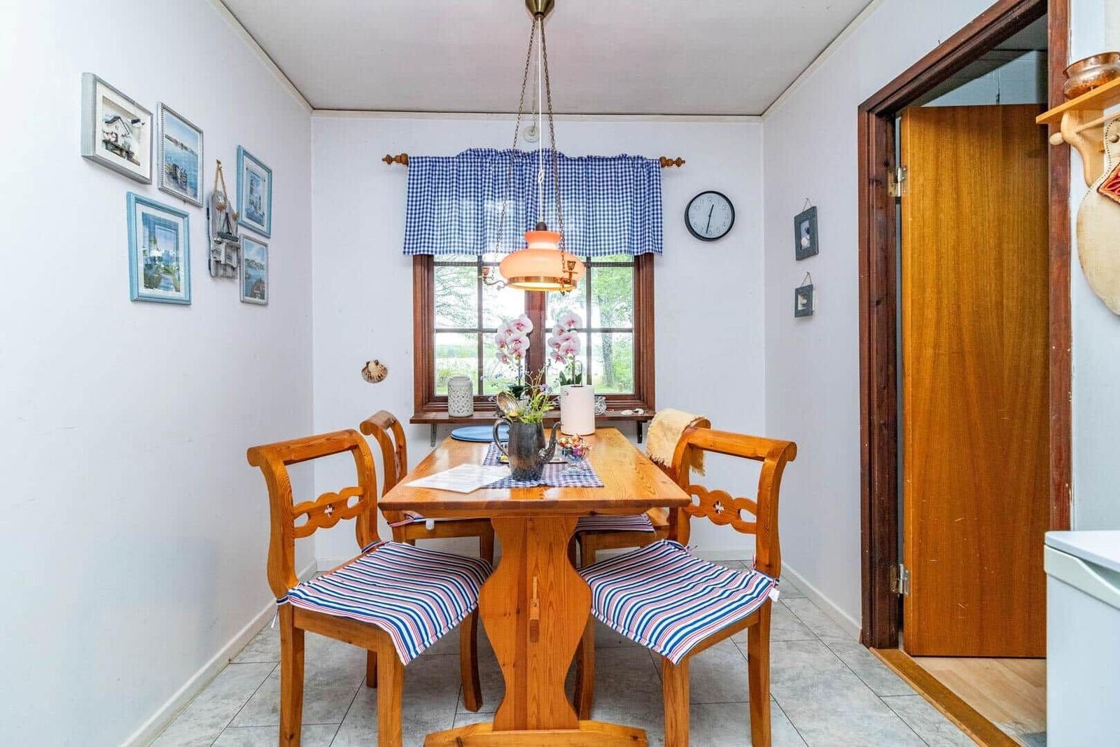 Esszimmer mit Holztisch, vier Stühlen und Fenster mit blau-weißem Vorhang.