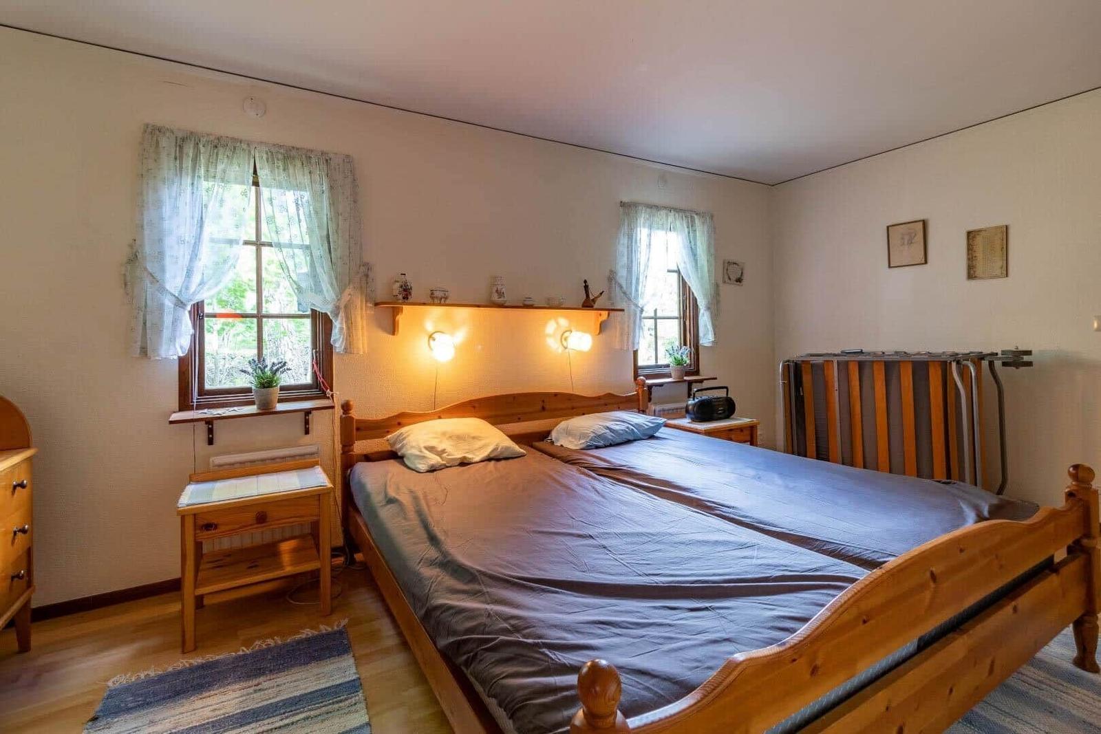 Schlafzimmer mit Holzbett, zwei Fenstern und Nachttischen.
