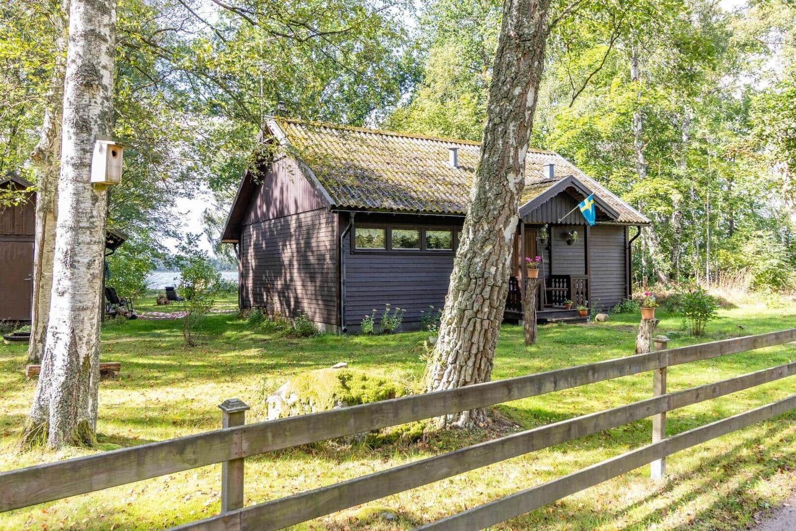 Holzhütte mit Garten und Seeblick, umgeben von Bäumen und einem Zaun.