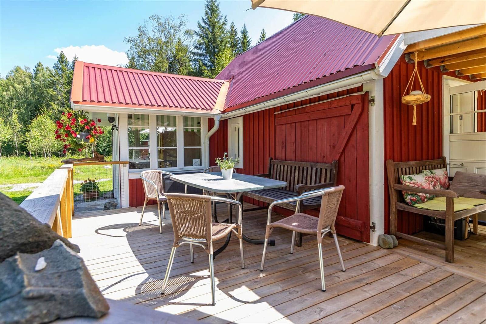 Terrasse mit Tisch, Stühlen und Sitzbank vor rotem Haus mit rotem Dach.