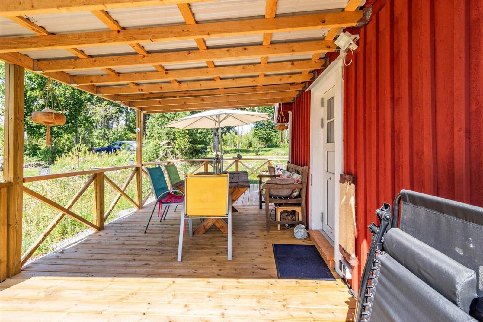 Terrasse mit Tisch, Stühlen und Sonnenschirm neben rotem Container.
