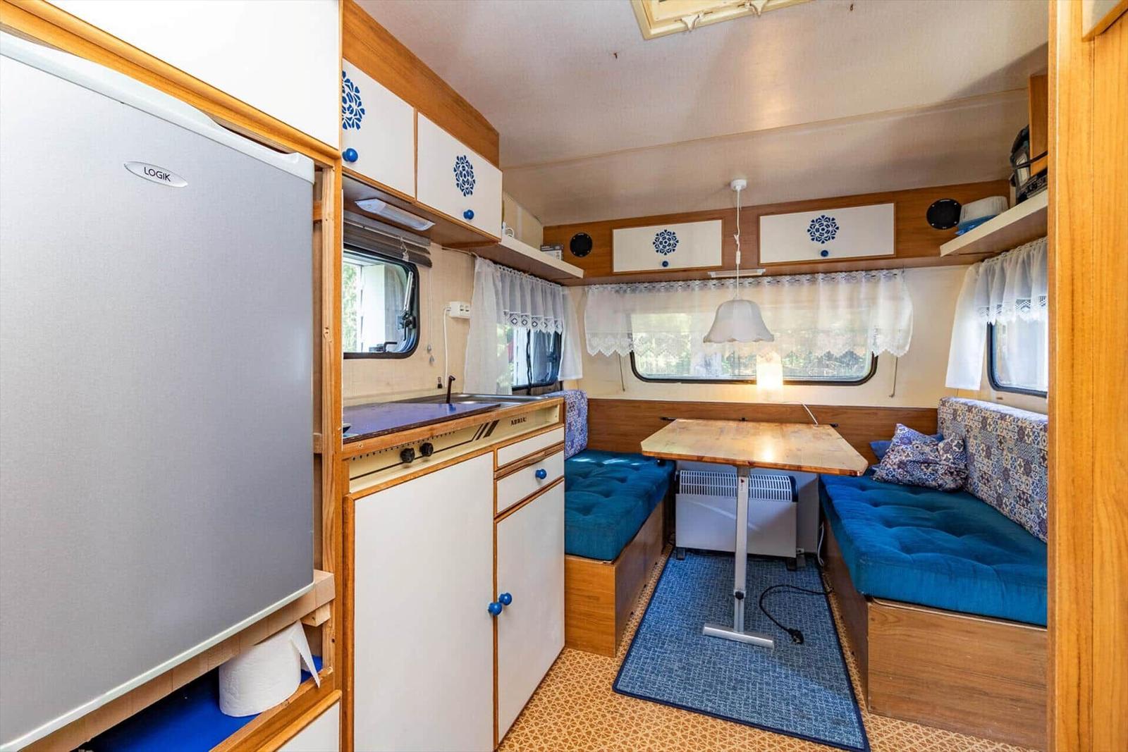Küche mit Kühlschrank, Tisch und Sitzbank mit blauen Kissen.