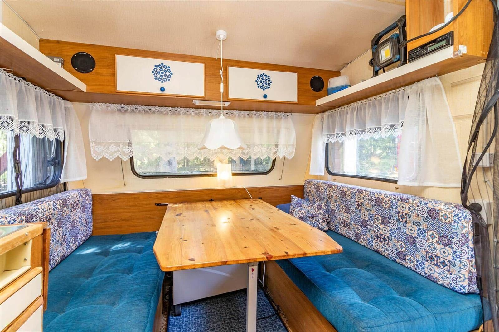 Sitzbereich mit Tisch und blauen Polstern. Fenster mit weißen Vorhängen.