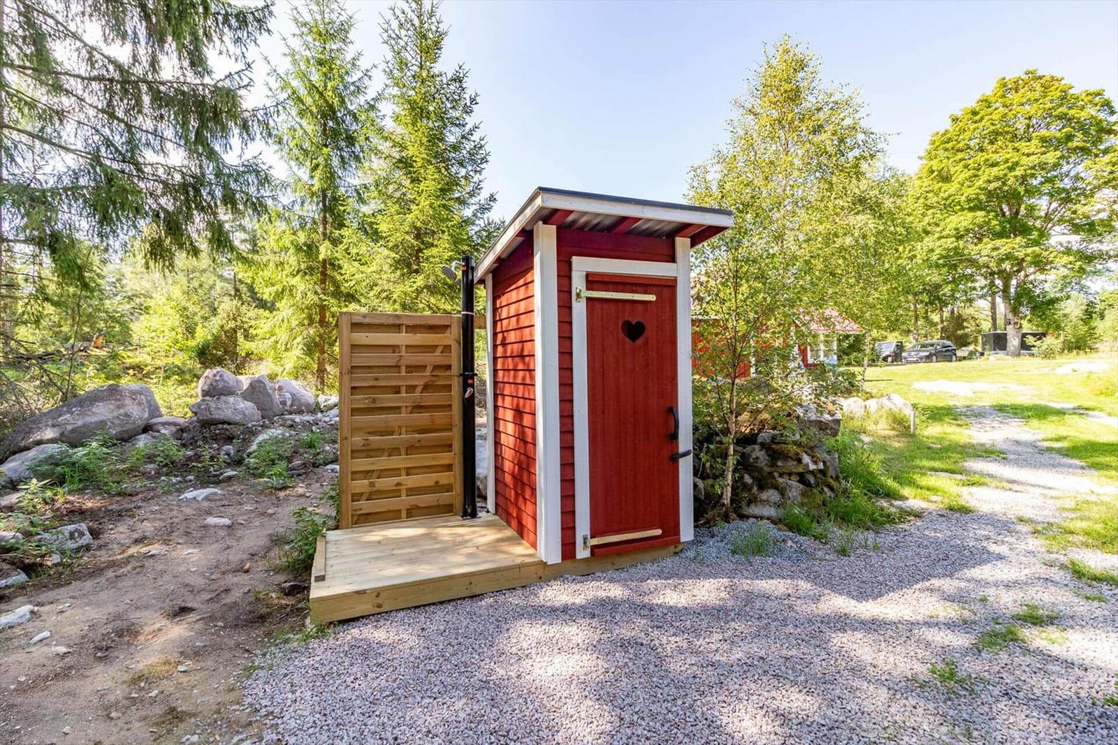 Rotes Holzbadhaus mit Herzförmigem Fenster und Dusche im Freien.