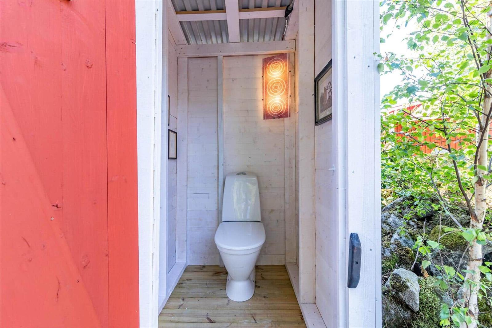 Hinter einem roten Tor befindet sich eine Toilette mit Holzboden und einer Wandlampe.