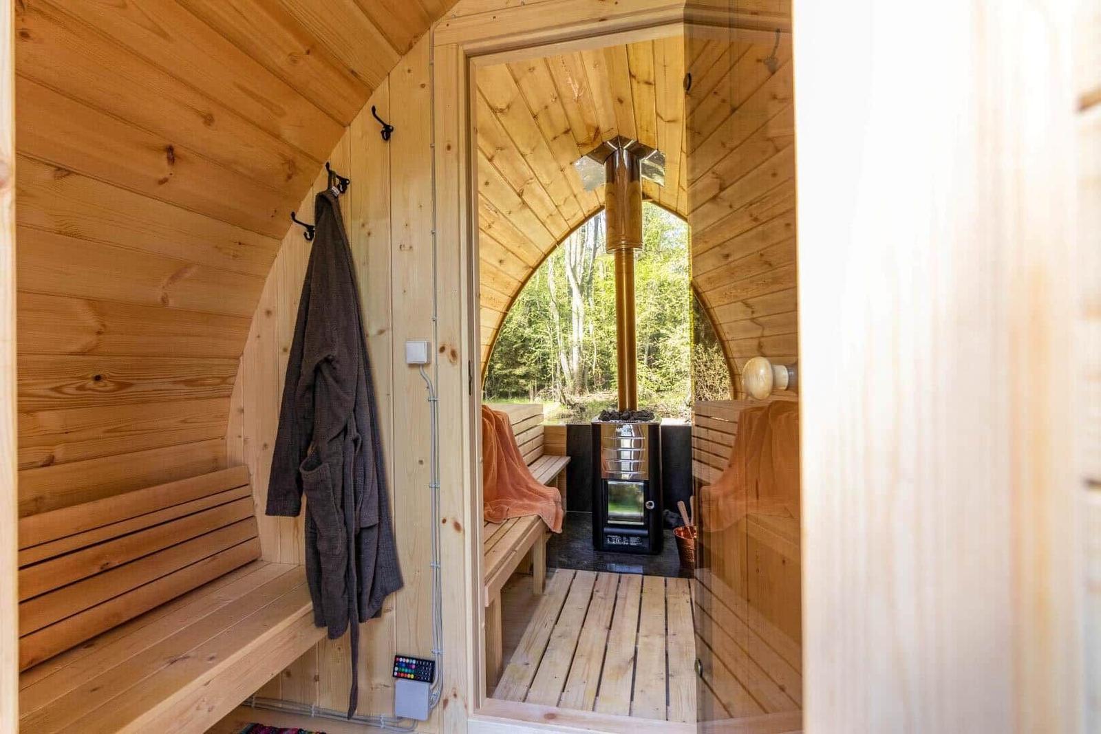 Holzsauna mit Sitzbänken, Ofen und Blick in den Wald.