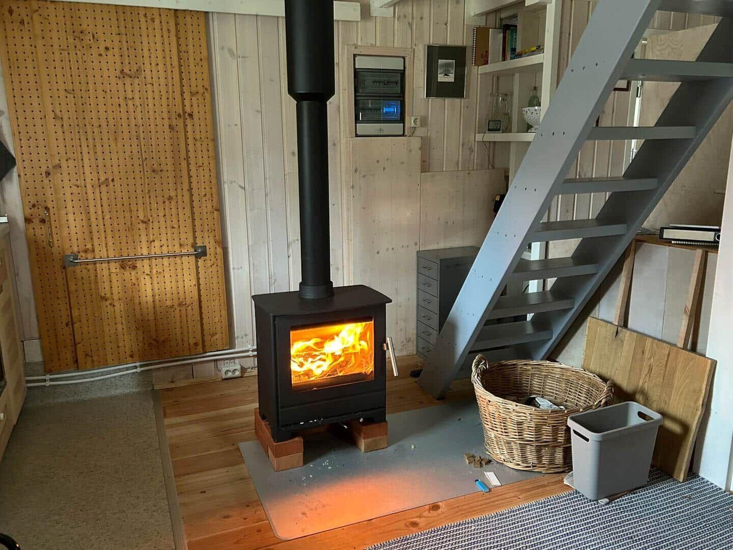 Kaminofen mit brennendem Feuer, Holztreppe und Korb im Raum.