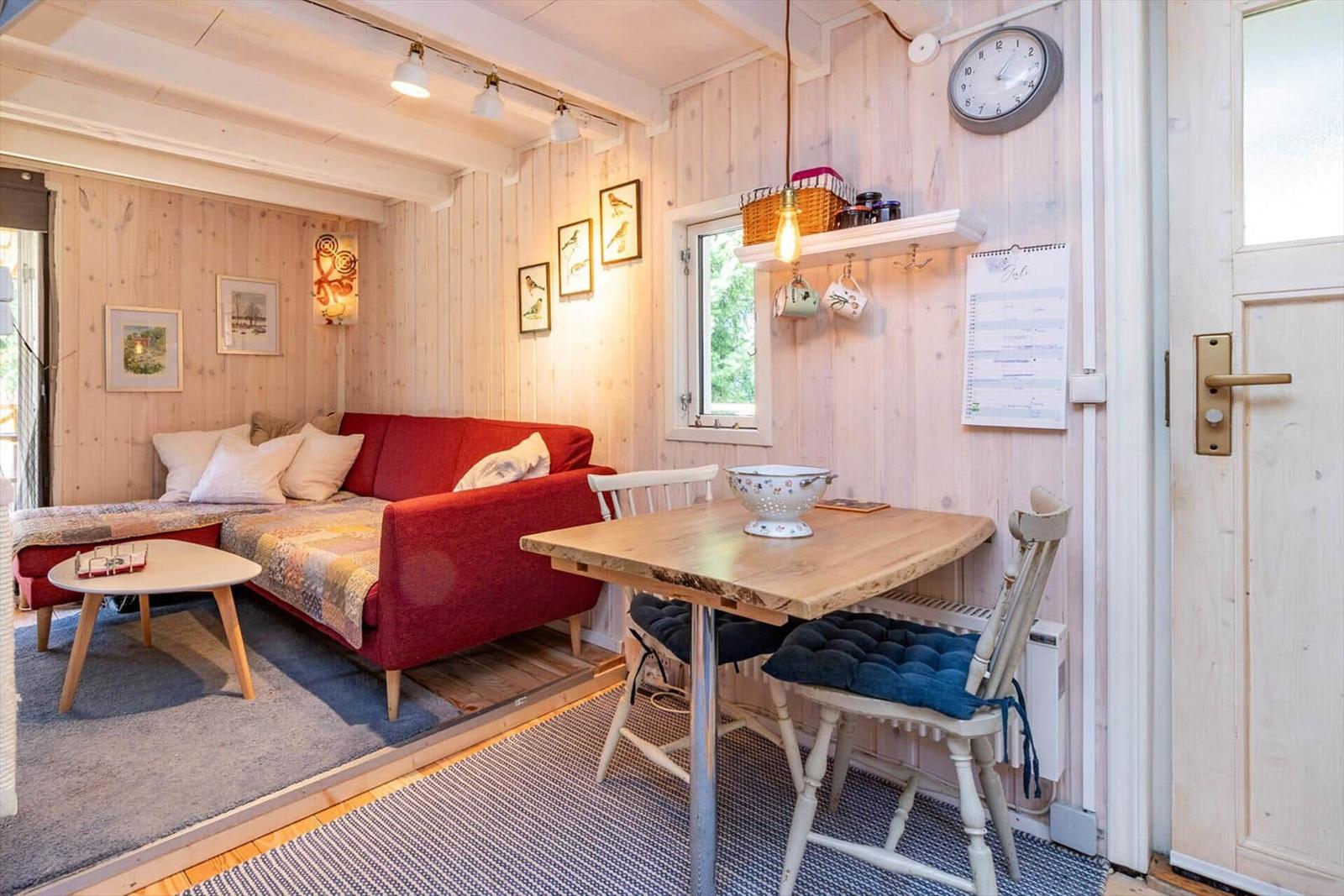 Ein Raum mit rotem Sofa, Holztisch und Stühlen, Wandbilder und einer Uhr.