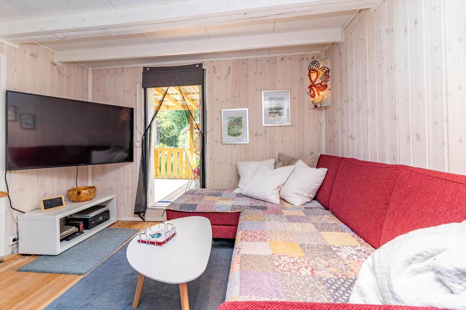 Ein Wohnzimmer mit rotem Sofa, Fernseher und Blick auf die Terrasse.