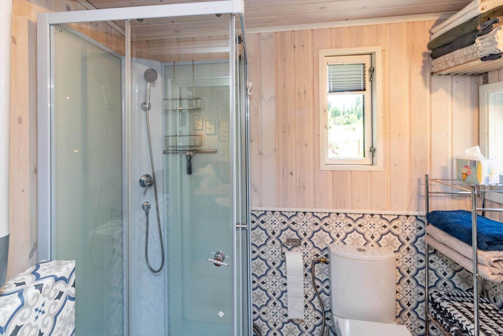 Badezimmer mit Dusche, Toilette und Fenster. Wände aus Holz und Mosaikfliesen.