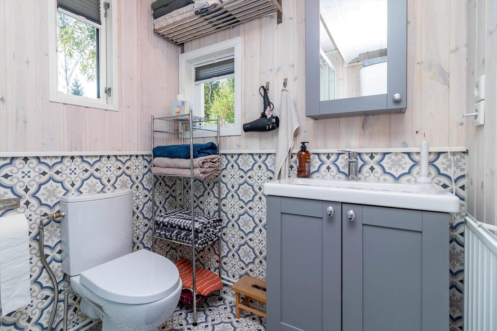 Badezimmer mit Toilette, Waschbecken und Badewannenbereich. Holzwände und Mosaikfliesen.