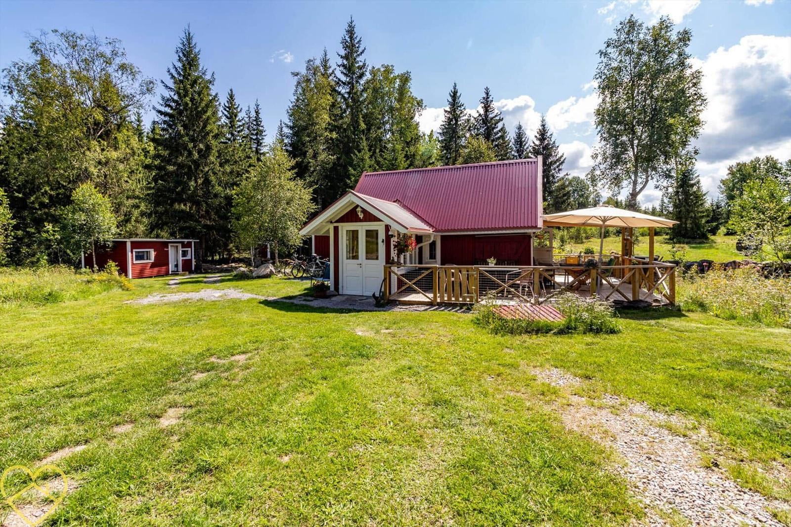Rotes Haus mit Terrasse und Grillplatz im grünen Garten.
