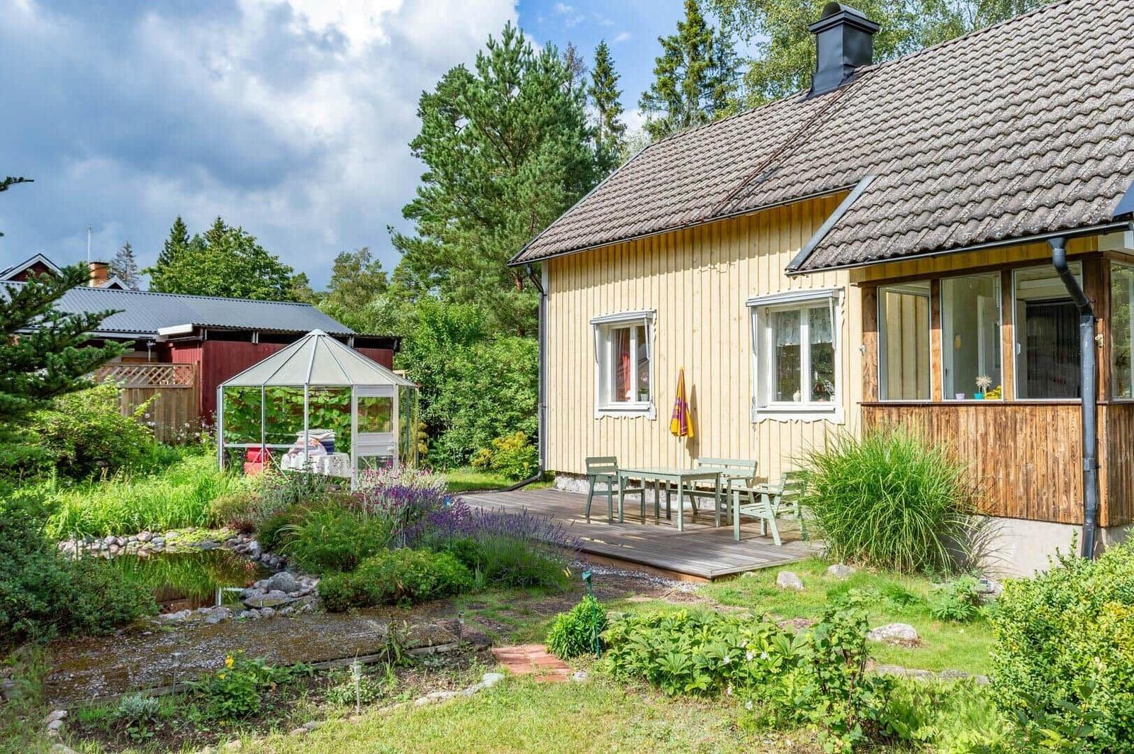 Haus mit Terrasse, Garten und Gewächshaus. Holzhaus mit Dach und Fenstern.