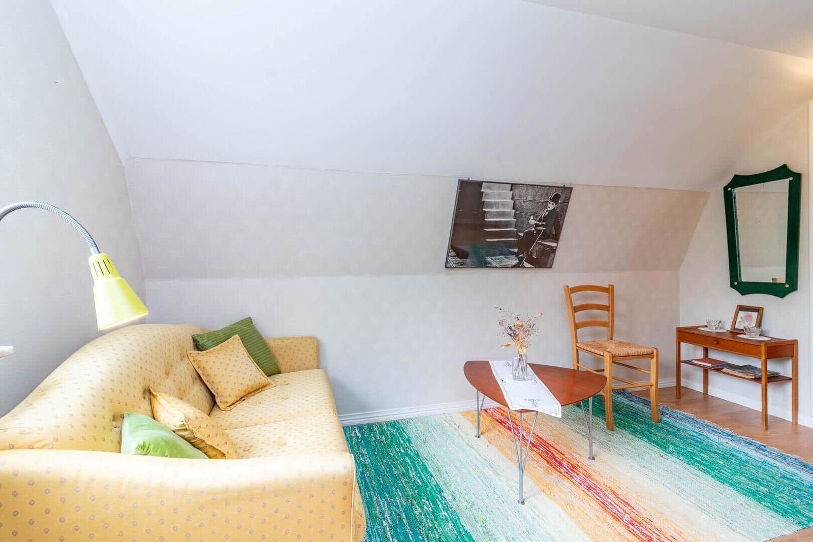 Ein Wohnraum mit Sofa, Stuhl, Tisch und Teppich unter schrägen Decken.