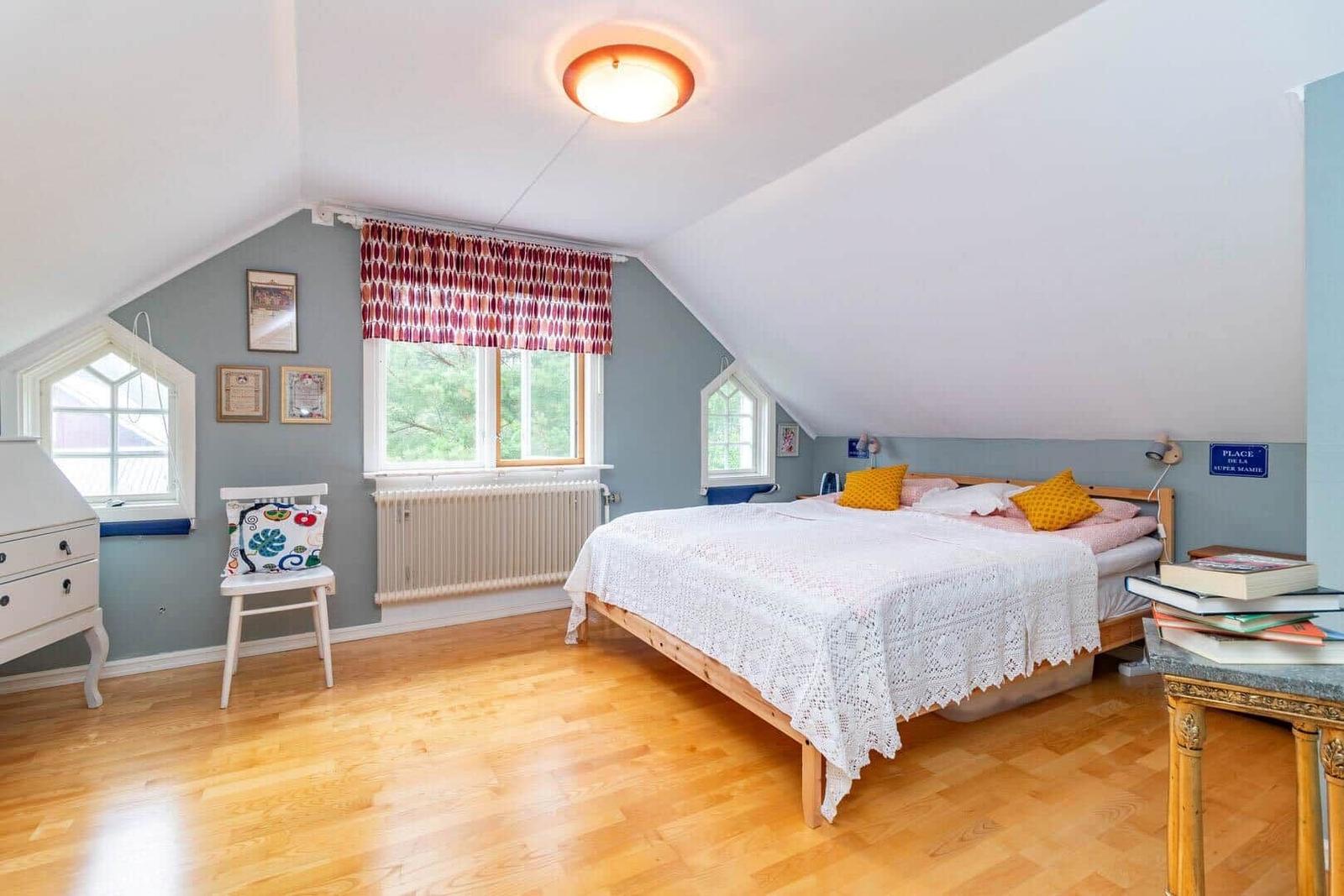 Schlafzimmer mit Dachschrägen, Holzboden und Bett mit weißer Tagesdecke.