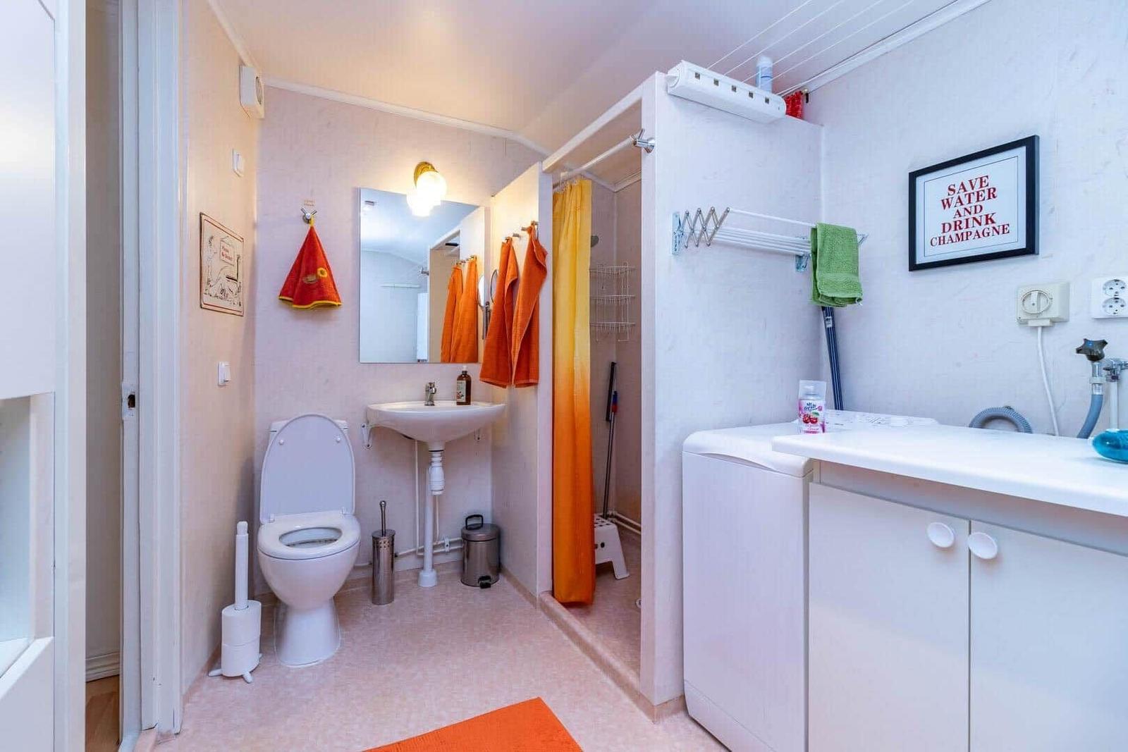 Badezimmer mit Toilette, Waschbecken und Dusche. Orange Handtücher und Fliesen.