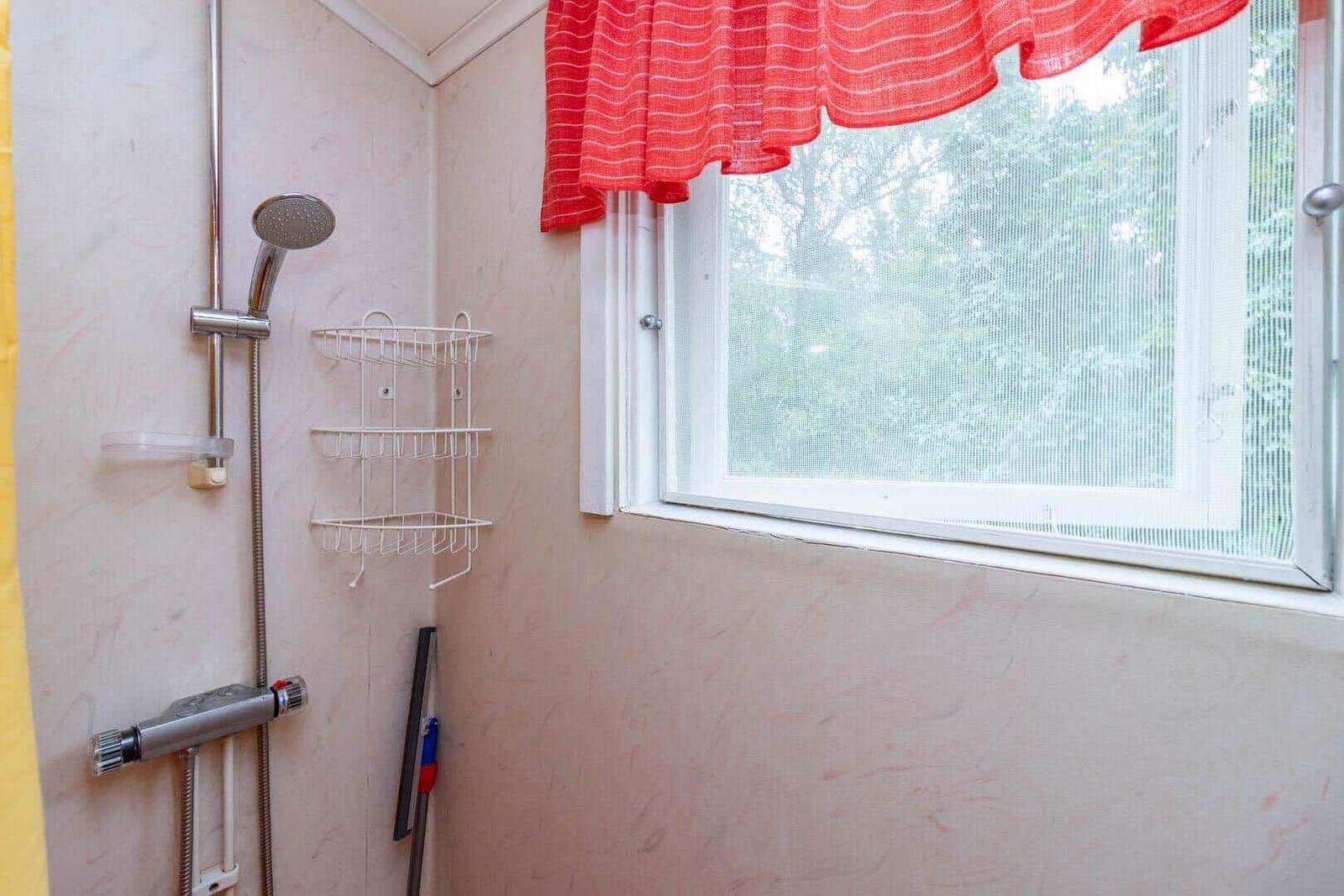 Bad mit Dusche, Fenster und rotem Vorhang.