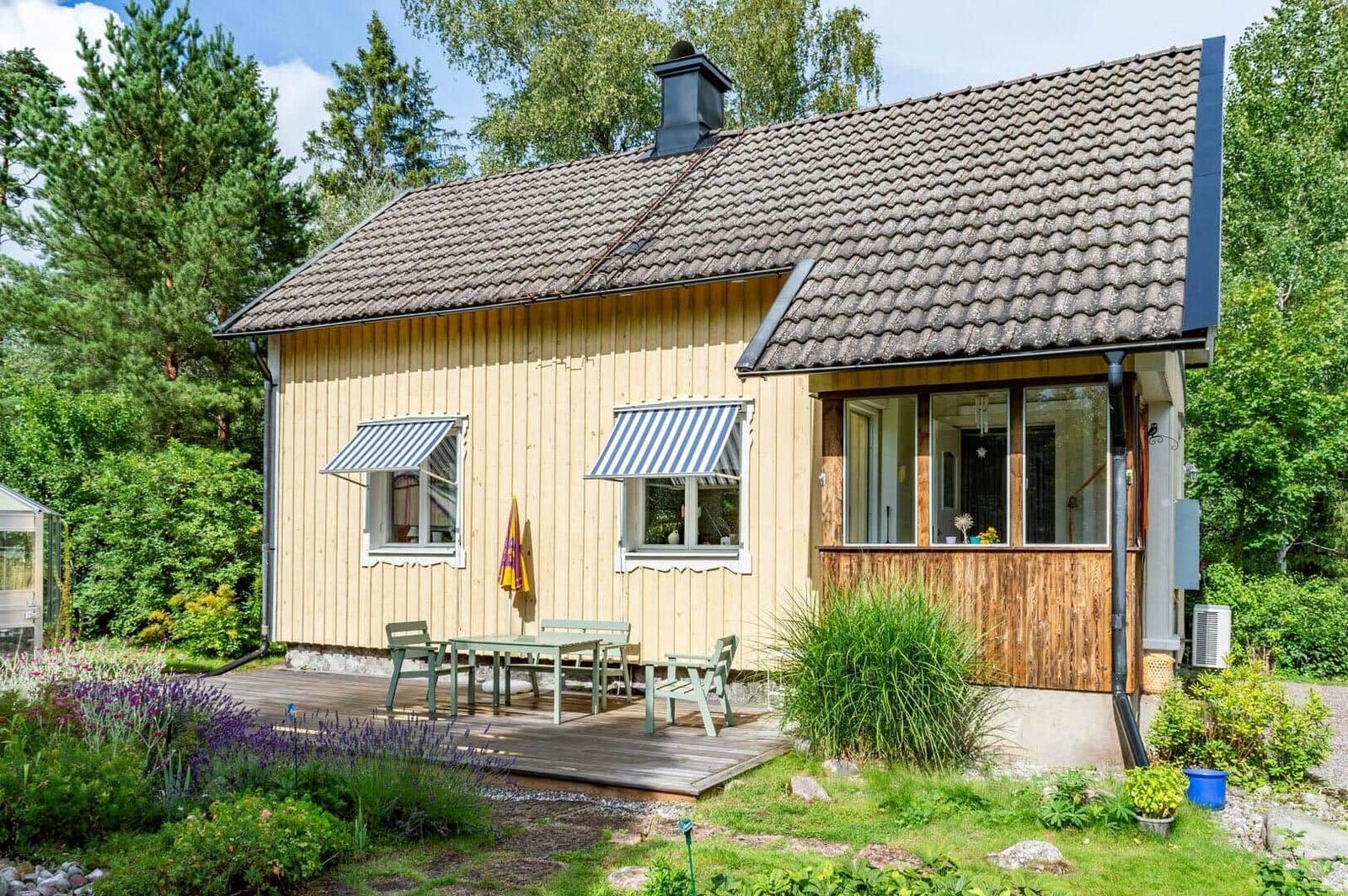 Haus mit Holzfassade, Terrasse und Garten. Blaue Markisen über Fenstern.