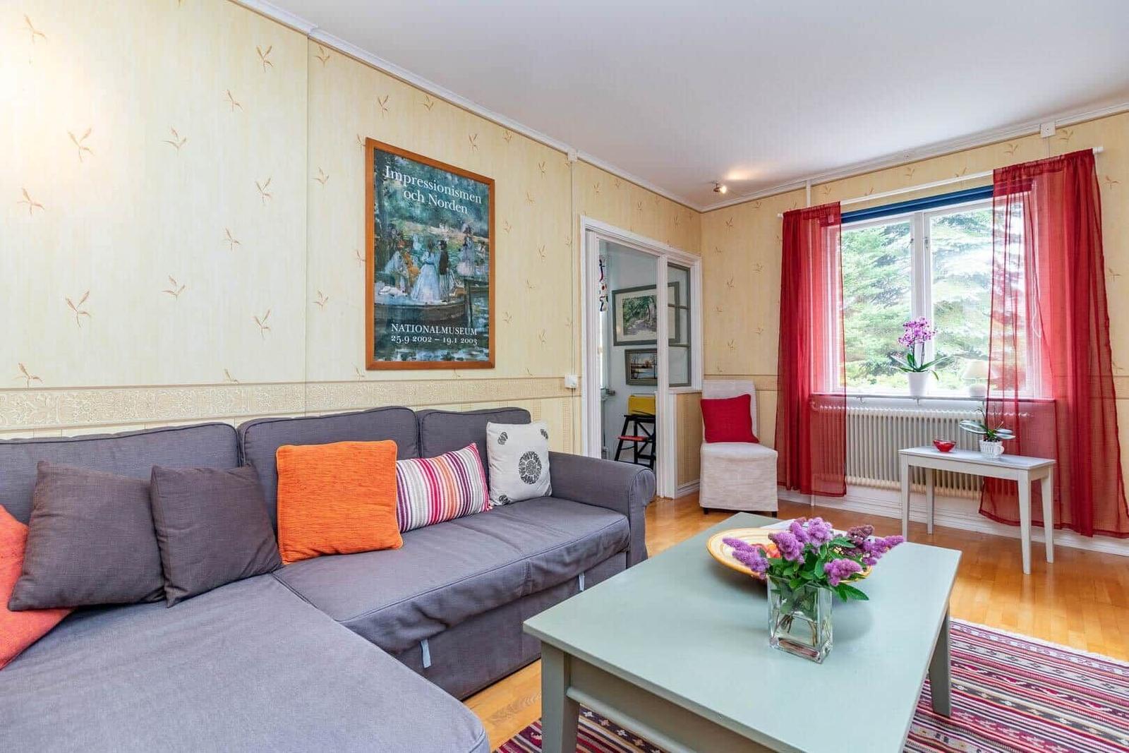 Wohnzimmer mit Sofa, Couchtisch und Fenster mit roten Vorhängen.
