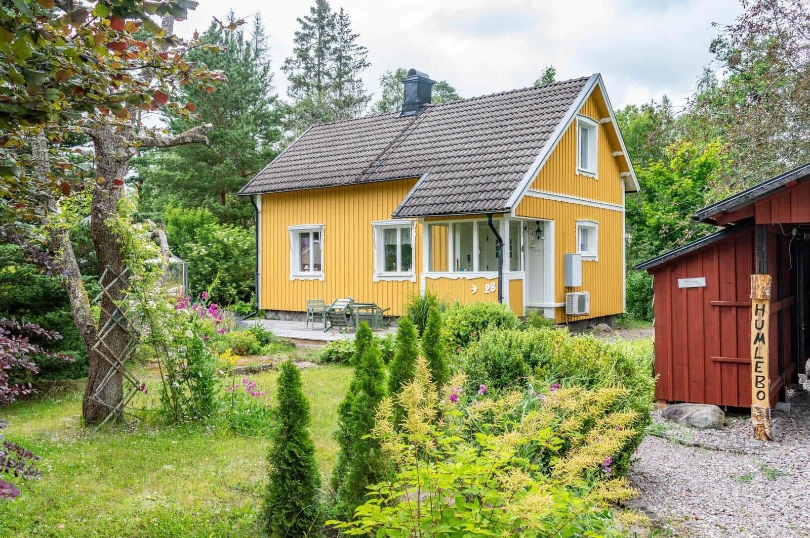 Gelbes Haus mit Terrasse und Garten. Neben einem roten Schuppen.