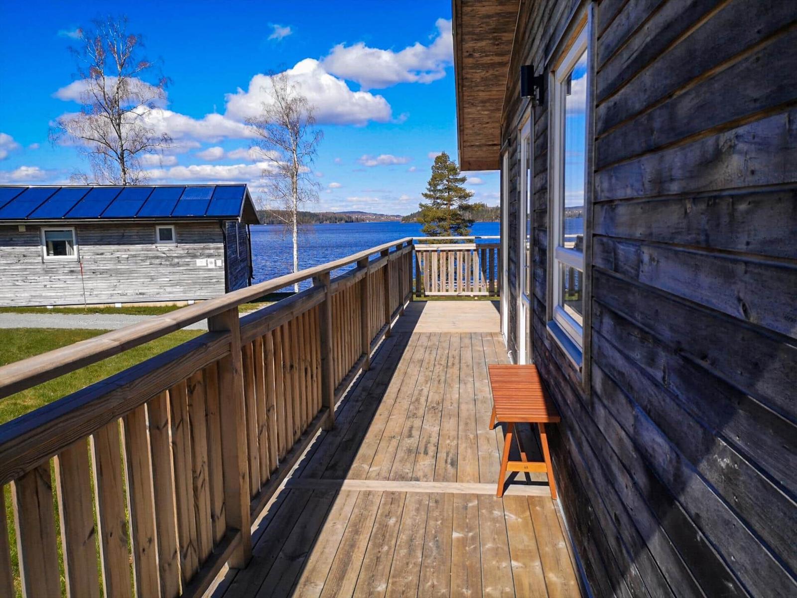 Holzterrasse mit Blick auf See und Himmel. Holzbank und Fenster sichtbar.