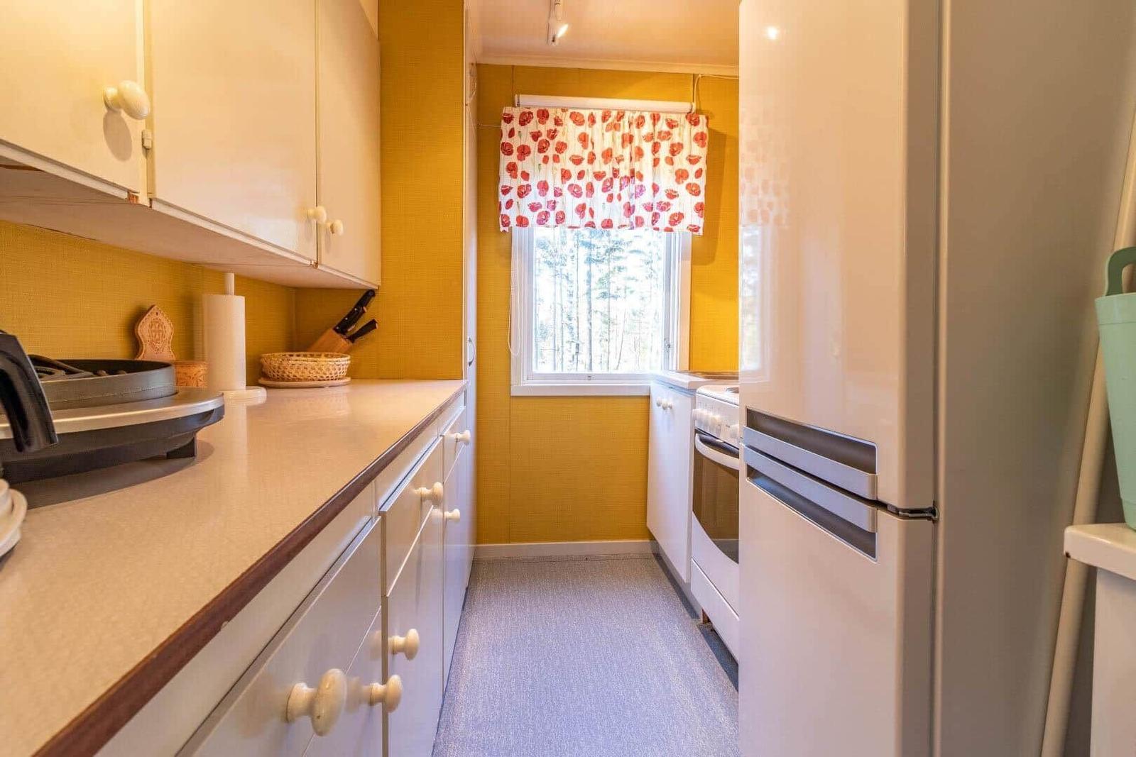 Küche mit gelben Wänden, weißen Schränken und Fenster mit Blumenrollo.