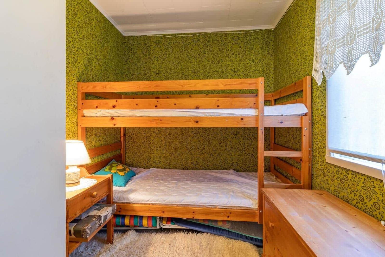 Zimmer mit Holz-Etagenbett, grünem Tapeten und Nachttisch mit Lampe.