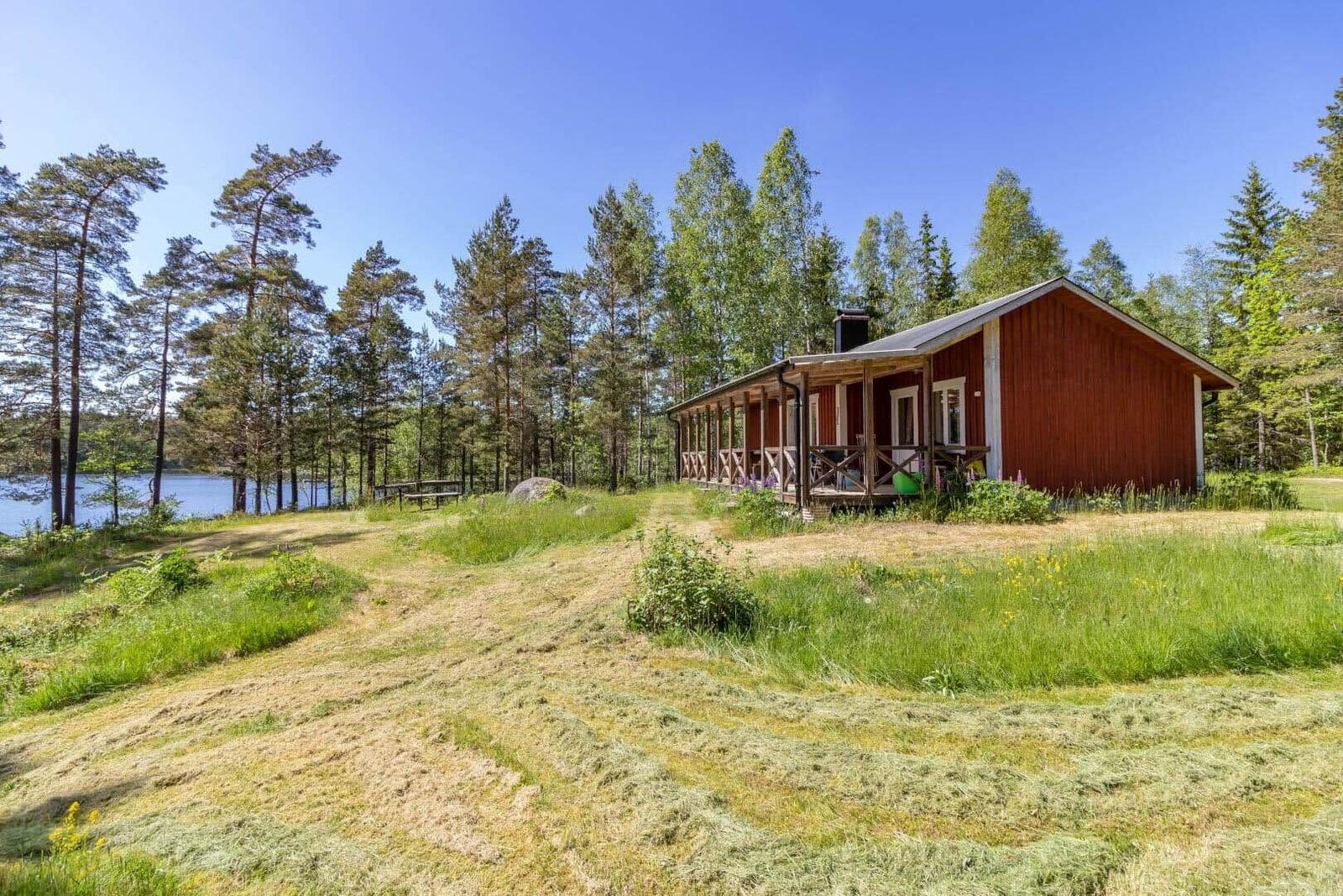 Rotes Holzhaus mit Veranda, umgeben von Wald und See.