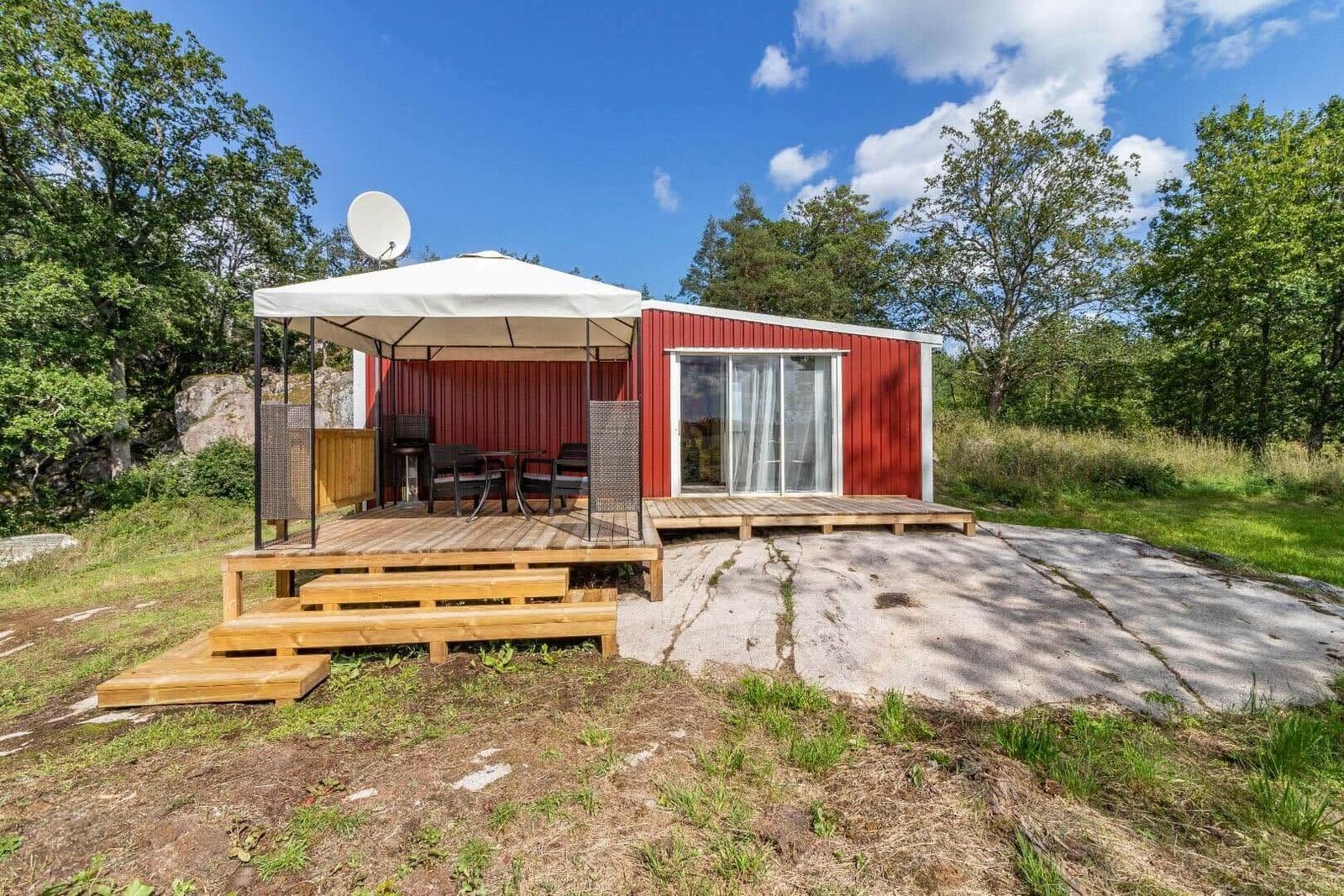 Rotes Gartenhaus mit Terrasse, Sonnenschutz und Satellitenanlage.