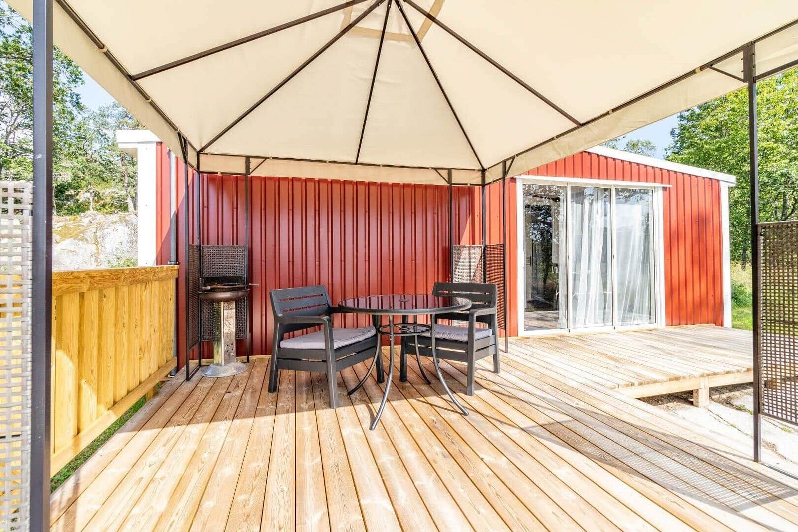 Terrasse mit Pavillon, Tisch, Stühlen und Grill. Rotes Gebäude mit Glasfront.